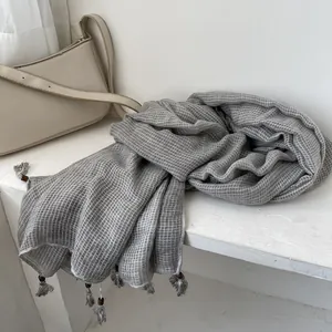 Dettaglio della sciarpa in cotone e lino grigia con nappe rustiche e perle di legno