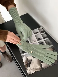 Detail of light green cable knit wool glove with leather logo tag and gold button decor