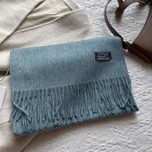 Detail of blue-grey wool scarf featuring soft cashmere texture and woven quote label