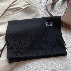 Detail of soft 100% pure wool black scarf featuring fringe edges and woven fabric label