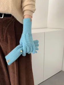 Detail of sky blue wool blend knit gloves featuring cable knit patterns and a metal logo button