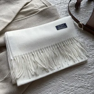 Detailed close-up of white 100% wool scarf featuring elegant tassels and a woven label