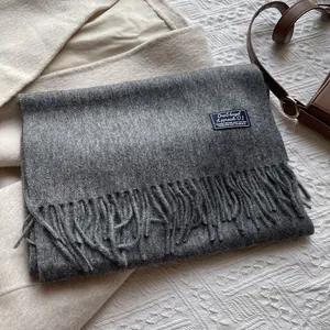 Detail shot of a dark grey wool scarf with fine tassels and a minimalist brand label