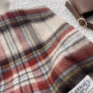 Close-up of wool plaid scarf texture with a brand tag on white ripple background