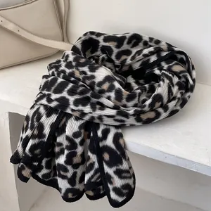 Detailed view of leopard print knit scarf with black stitched edges on a white surface