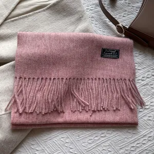 Detailed view of pink wool scarf with fringe edges and brand label on textured fabric