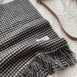Detail of wool houndstooth scarf featuring long fringe tassels and brand logo label