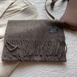 Close-up of a dark brown wool scarf with tassel details and a blue woven label