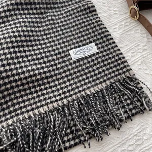 Detail of wool houndstooth scarf with fringe edge and white brand label on white texture