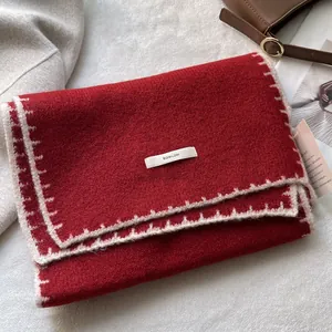 Dettaglio di sciarpa in maglia rossa con cuciture bianche ed etichetta in tessuto