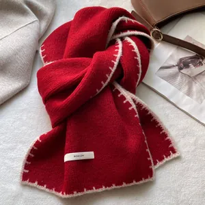 Dettaglio di sciarpa in maglia rossa con cuciture a contrasto ed etichetta in tessuto