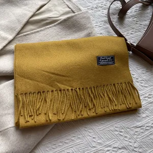 Detail of mustard yellow wool scarf featuring fringe ends and a chic decorative fabric label