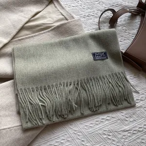 Detail of sage green wool scarf with fringe edges and rectangular woven brand tag