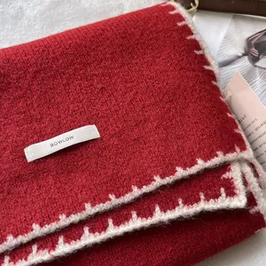 Dettaglio della sciarpa in maglia rossa spessa con bordi a zigzag e marchio BOWLOW