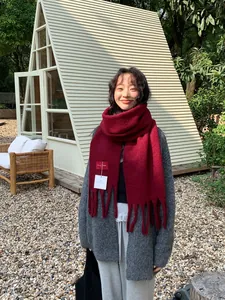 Detail of burgundy wool scarf with chunky tassels and brand label in outdoor setting