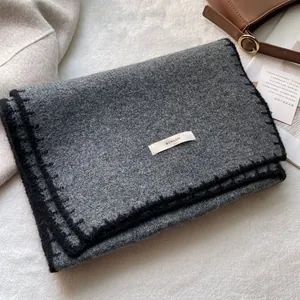 Dettaglio ravvicinato della sciarpa in maglia grigio scuro con bordo nero e etichetta
