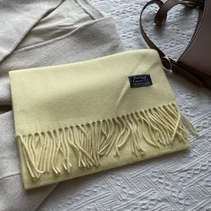 Detailed view of light yellow wool scarf with fringe tassels and woven brand label