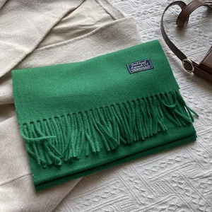 Detail shot of a forest green wool scarf featuring fringed edges and a black woven label