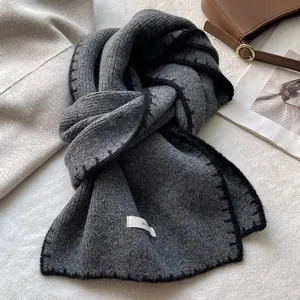 Dettaglio di sciarpa in maglia grigio scuro con cuciture nere e etichetta bianca del marchio