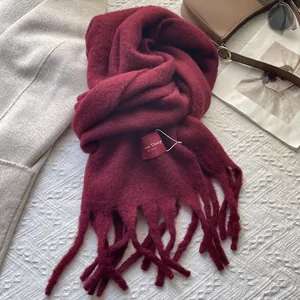 Close-up of thick dark red winter scarf with long tassels on white lace texture
