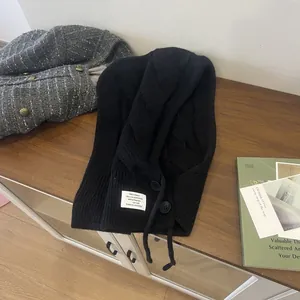 Detail der schwarzen Balaclava-Strickmütze mit Knöpfen auf einem Holzschrank