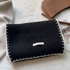 Dettaglio borsa in maglia nera con cuciture a contrasto bianche ed etichetta tessuta