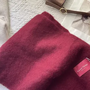 Close-up of burgundy wool scarf with plush texture and woven brand label detail