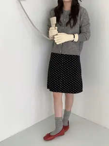 Gros plan de gants en tricot blanc cassé portés avec cardigan gris et ballerines rouges