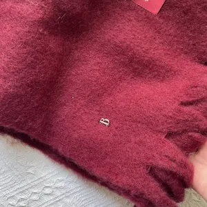 Macro detail of wine red wool scarf fabric showing soft brushed texture and metal B logo