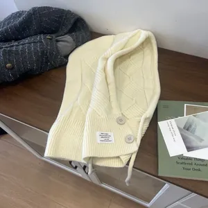 Detail der cremefarbenen Strick-Balaclava mit Knopfverschluss und dekorativem Etikett