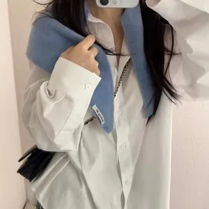 Détail du châle en laine tricoté bleu clair avec étiquette sur une chemise blanche