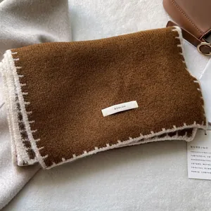 Dettaglio di sciarpa in maglia marrone con cuciture bianche e etichetta del marchio