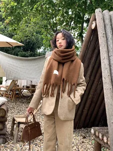 Detail of a brown knit scarf with thick fringe and rectangular woven brand tag