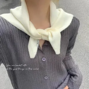 Gros plan d'un foulard triangulaire en tricot blanc noué sur un cardigan gris côtelé