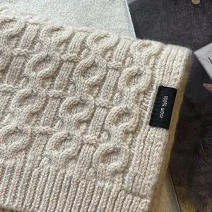 Detail showing 100% wool material tag on a beige cable-knit scarf with soft texture