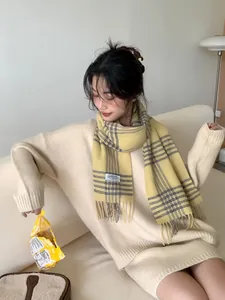Detail of yellow plaid wool scarf with fringes worn over a beige knitted cardigan