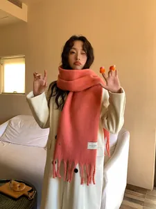 Close-up of a coral pink thick scarf with tassels on a white wool coat