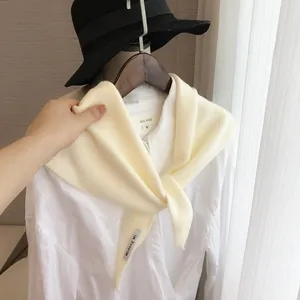 Détail d'un foulard triangle en tricot crème avec étiquette sur chemise blanche