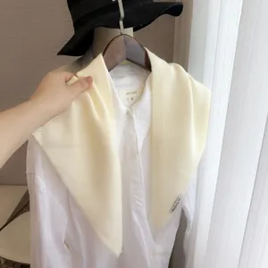 Détail d'un châle triangulaire en tricot crème sur une chemise blanche à col pointu