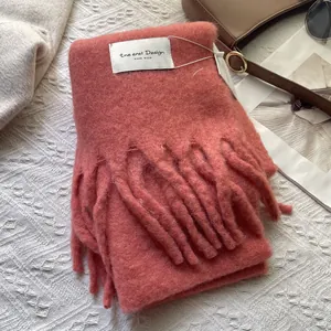 Close-up of pink wool scarf with handmade label and fringe on textured background
