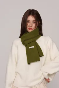 Close-up of grass green knit scarf showing the 100% wool material label and soft texture