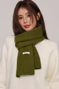 Detail of moss green wool scarf texture with 100% wool label on model in white sweater