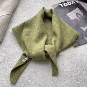 Détail d'un foulard triangulaire en tricot vert avec étiquette sur fond gris texturé
