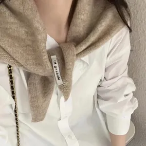 Détail de l'écharpe triangulaire en tricot camel avec étiquette sur chemise blanche