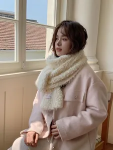 Detail showing soft white wool scarf texture with pink logo tag on pink wool coat