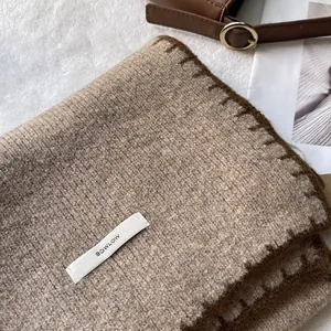 Dettaglio della sciarpa in maglia kaki con bordo marrone e etichetta del marchio su tessuto