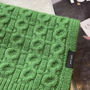 Detail view of green 100% wool scarf showing cable knit texture and material tag