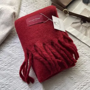 Detailed texture of burgundy knit scarf with long fringes and brand tag on fabric