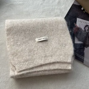 Close-up of oatmeal wool knit scarf featuring metal B logo and ERET-WOOL woven label