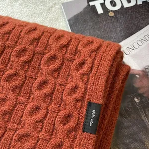 Detail of 100% pure wool scarf showing thick cable knit texture and material label